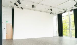 Nell Gwynne Studio - a large empty toom with glass walls and a large white wall on one side. There are floor to ceiling length black curtains which are drawn around the room. 