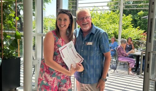 A man and woman stood smiling in The Courtyard Lounge The woman holds a certificate