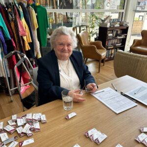 An elderly woman sits smiling at a table surrounded by name badges.