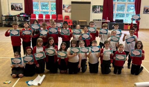 A group of children in school uniform smiling at the camera holding pictures of speech bubbles