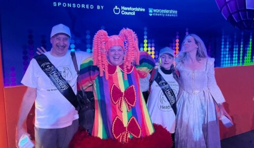 Four people stand in front of a screen smiling Two are in fancy dress