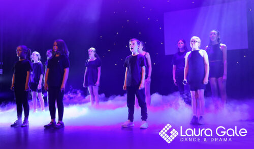 A group of children dressed all in black standing on a stage singing