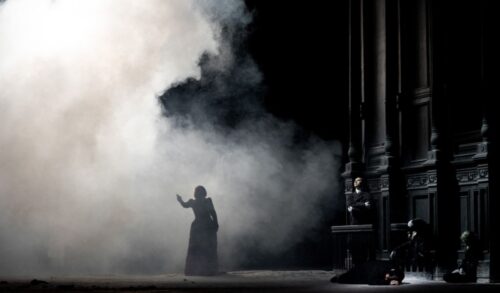 A figure performs on stage amongst a cloud of smoke