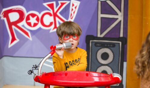 Little Play World  a young boy sits at a toy piano with the word rock behind him