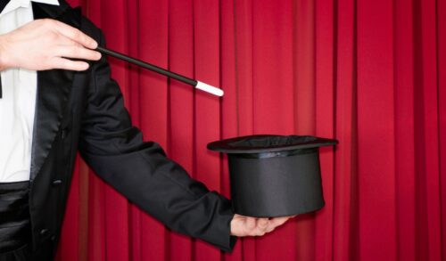 Mr Bamboozles Magic Show  a magician holds a wand over a hat in front of a red curtain