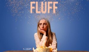 A woman sits in from of a cake with birthday candles looking worried. There is confetti above her head. Writing reads 'Fluff'