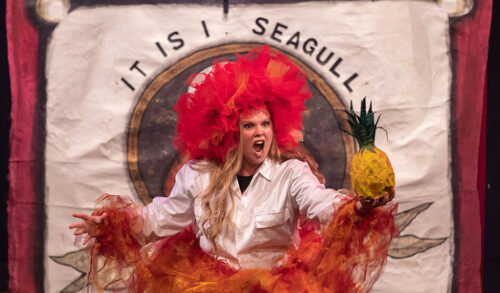 A woman with a red material headdress screams while holding a pineapple