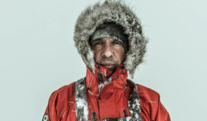 A close up of a man in a fur hooded coat, surrounded by snow.