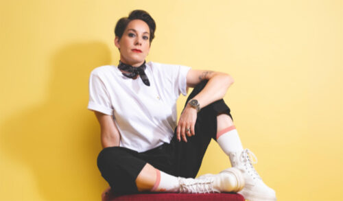 Suzi Ruffell sits against a yellow wall