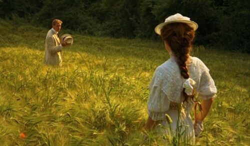 A man and a woman stand in a green field of flowers They are looking at one another from a distance