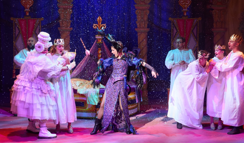 A pantomime villain waves a wand at the pantomime Dame and Queen who holds a baby