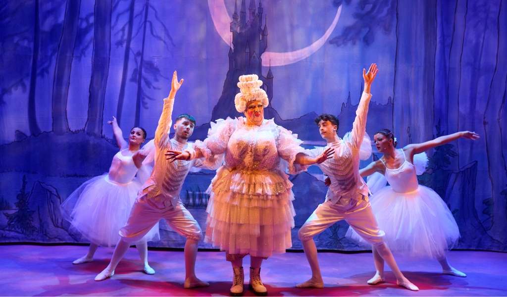 A pantomime Dame and four characters dressed as ballerinas dance on stage.