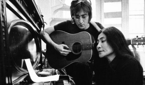 A black and white photo of John Lennon playing a guitar and Yoko Ono playing the piano