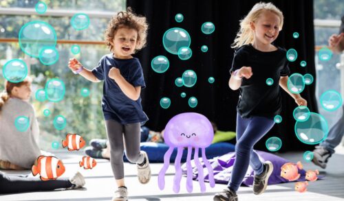 Two young children running across a studio room smiling There are illustrations of bubbles fish and a jellyfish surrounding them